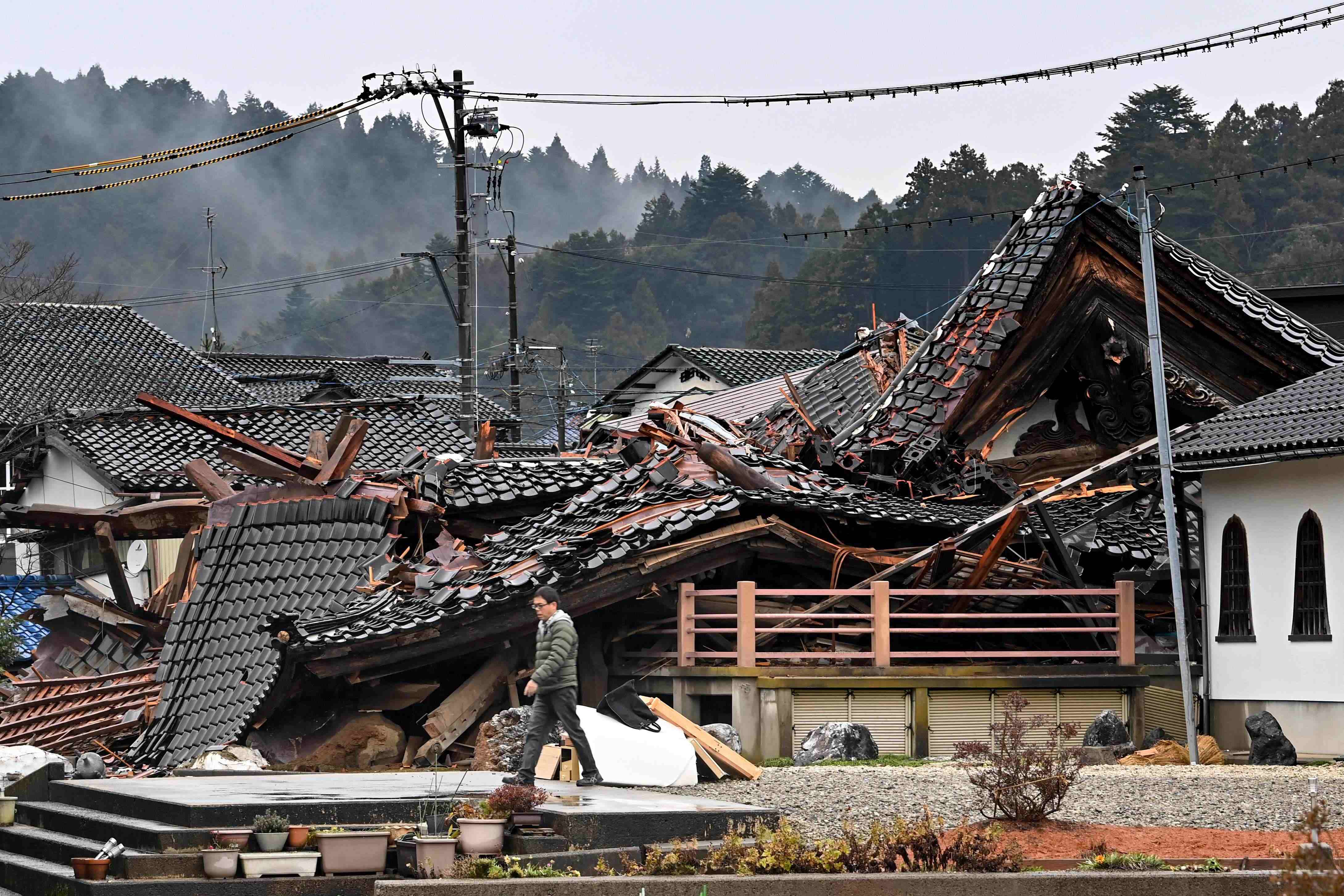 倒壊した家屋の前を通り過ぎる人＝2024年1月3日、石川県穴水町【AFP時事】