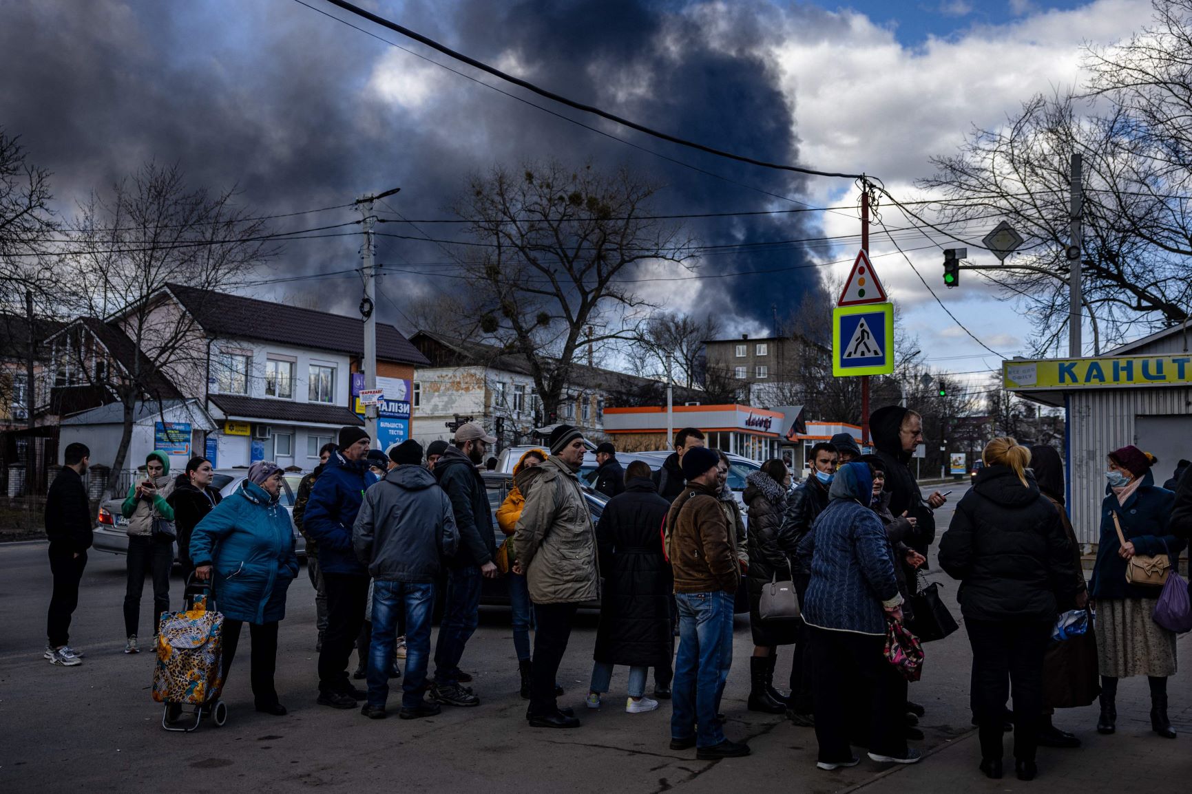 ロシア軍による給油所攻撃で黒煙が上がる中、スーパーに並ぶウクライナの人々＝2月27日AFP時事