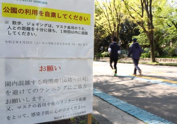 公園利用の自粛を求める掲示板の横をジョギングする人たち（２０２０年４月２５日撮影、東京・駒沢オリンピック公園）