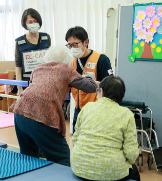 避難所で要介護者の立ち上がりを手伝う医療関係者＝３１日午後、石川県輪島市
