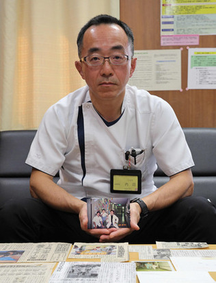 写真を手に取り、インタビューに応じる医師の内田恵一さん=2月26日、三重県四日市市