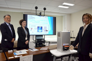 アルファ線がん治療薬用の小型分析システム(手前の箱形)を開発した日本原子力研究開発機構の瀬川麻里子マネジャー(中央)や量子科学技術研究開発機構の西中一朗上席研究員(左)ら=18日、東京都千代田区の原子力機構東京事務所
