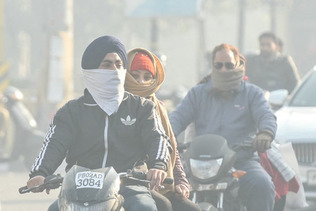 大気汚染の中、布で顔を覆い通勤する人々＝２０２３年１２月、インド北部アムリトサル（ＡＦＰ時事）